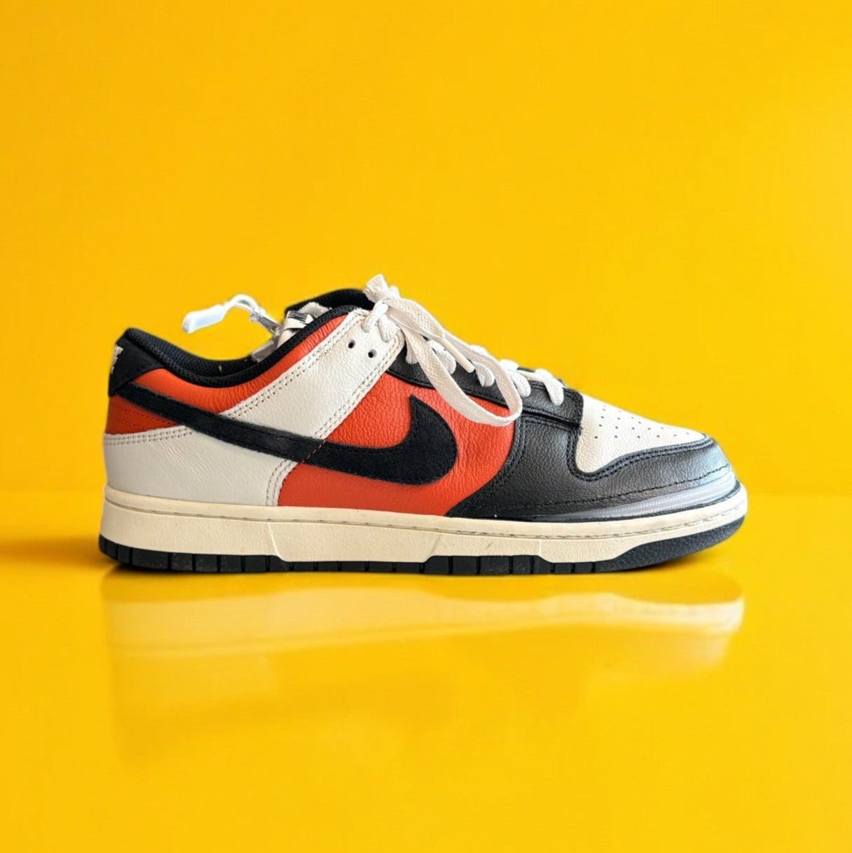 Black, orange, and white dunk low retro shoe with a zipper on a yellow background. The shoe is zipped shut