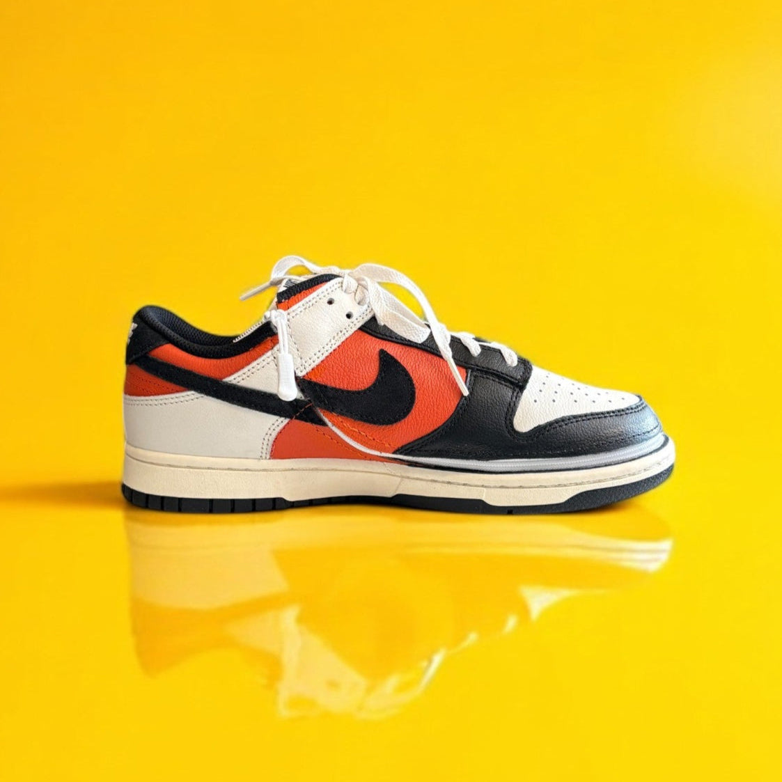 Black, orange, and white dunk low retro shoe with a zipper on a yellow background. The shoe is zipped shut