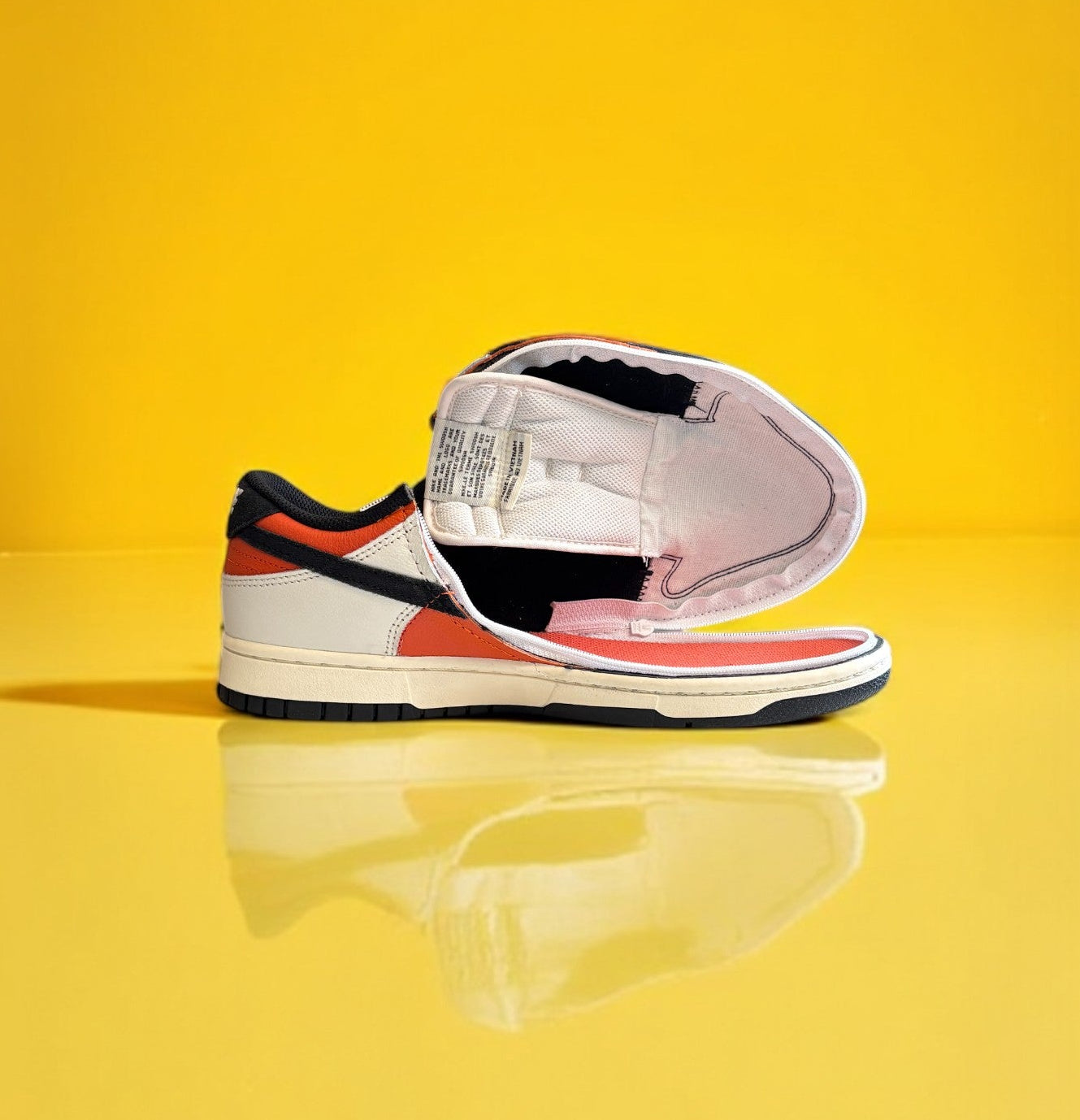 Black, orange, and white dunk low retro shoe with a zipper on a yellow background. The shoe is fully open