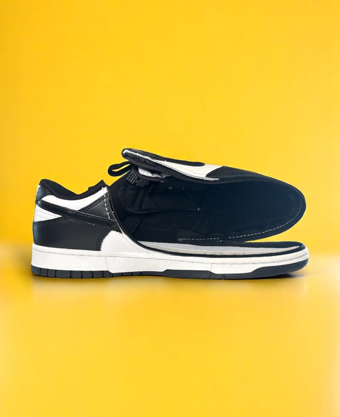 Black and white dunk low retro shoe with a zipper on a yellow background. The shoe is fully open