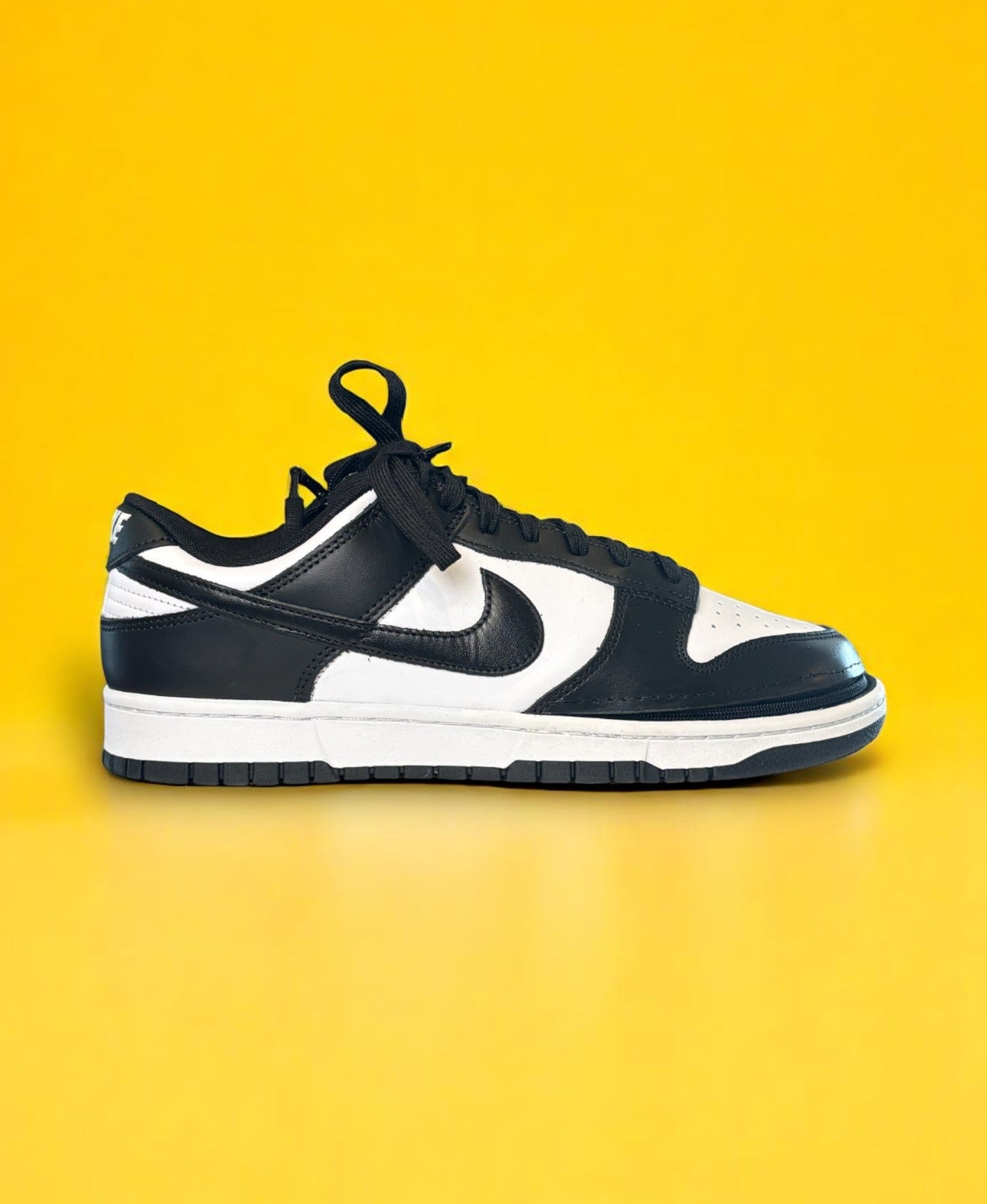 Black and white dunk low retro shoe with a zipper on a yellow background. The shoe is zipped shut
