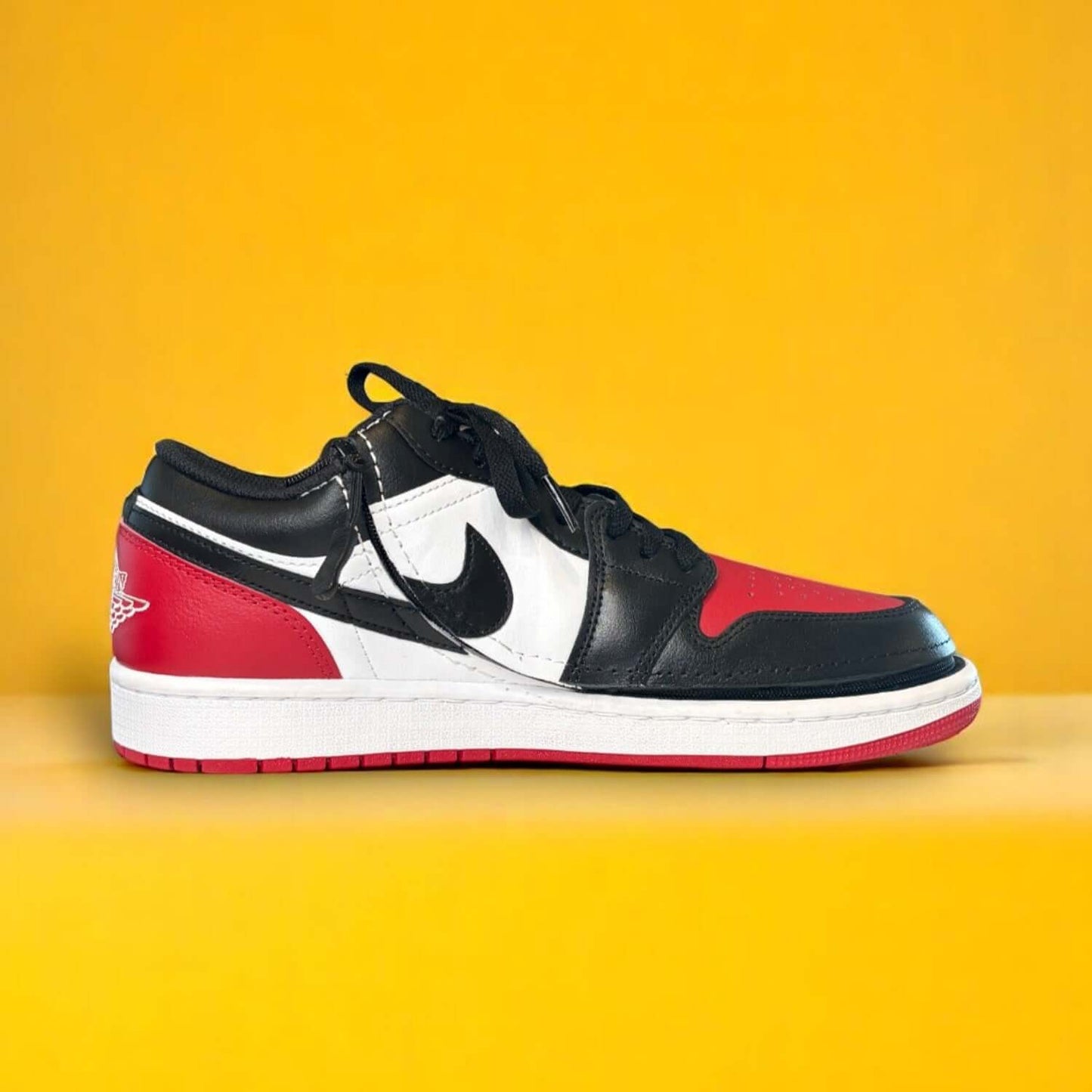 Black, white, and red shoe with a zipper on a yellow background. The zipper wraps around the shoe
