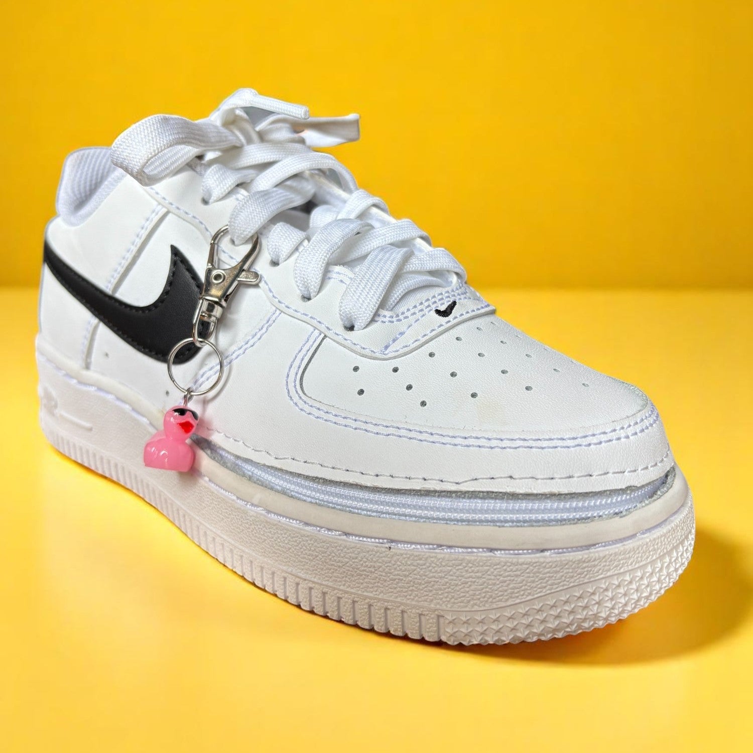 Pink duck charm on a White sneaker with black swoosh logo on a yellow background