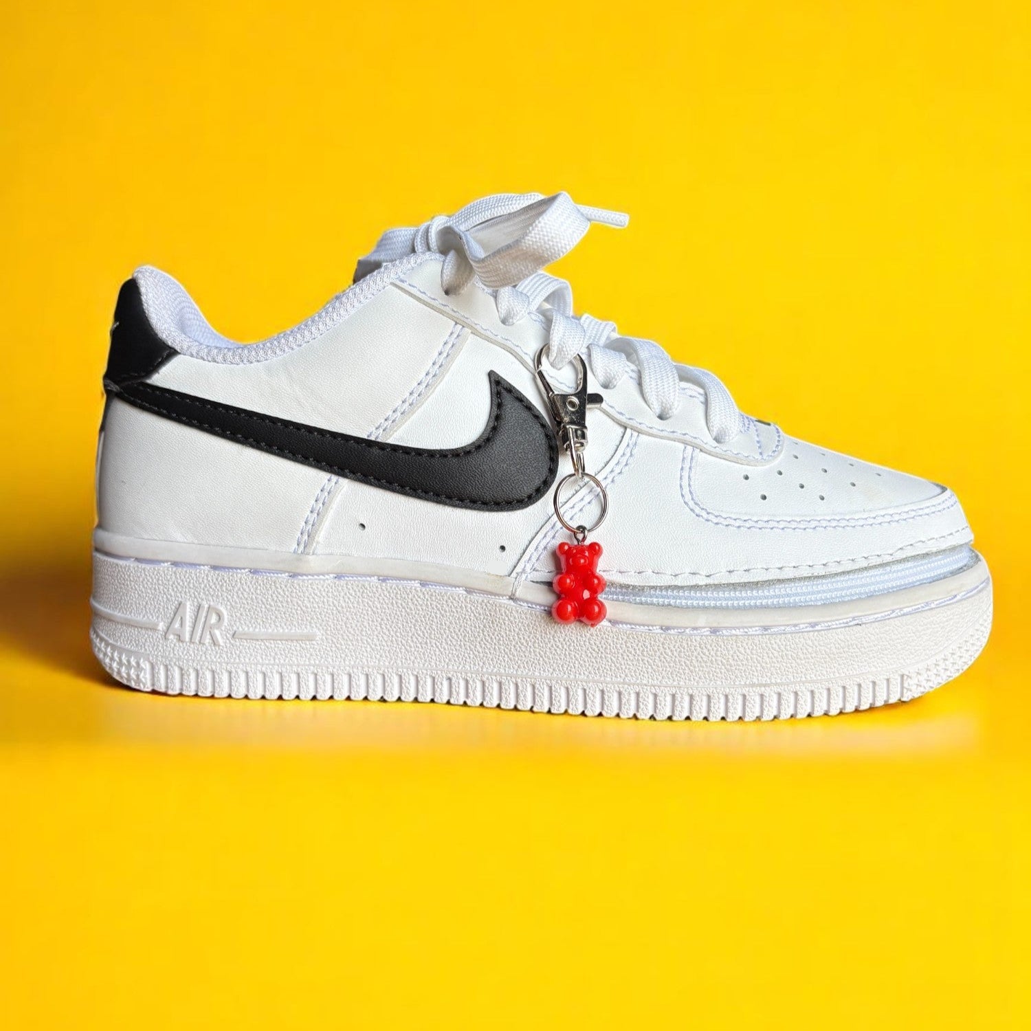 White Nike Air sneakers with a red gummy bear shoe charm, highlighting trendy shoe accessories.