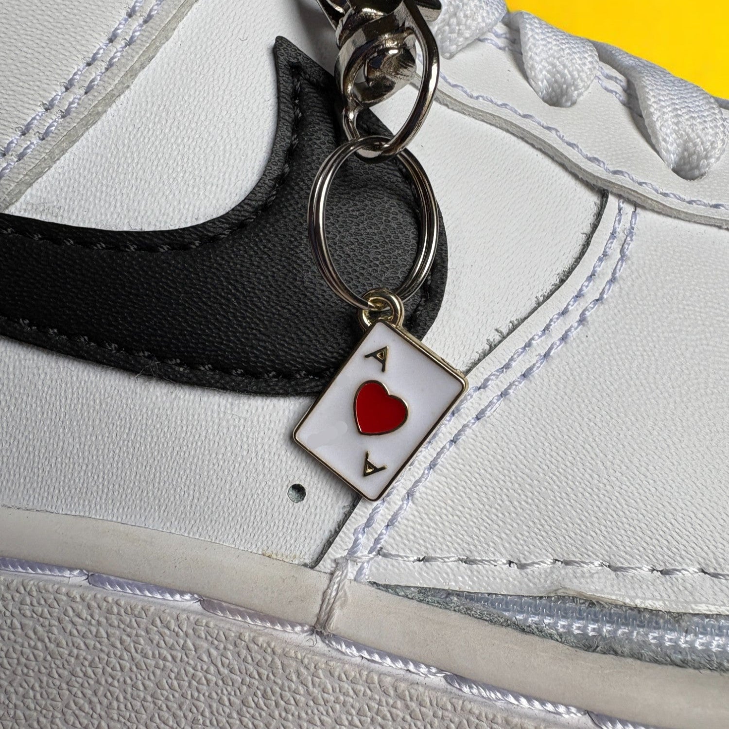 White sneaker with a keychain featuring a ace of hearts symbol on a yellow background