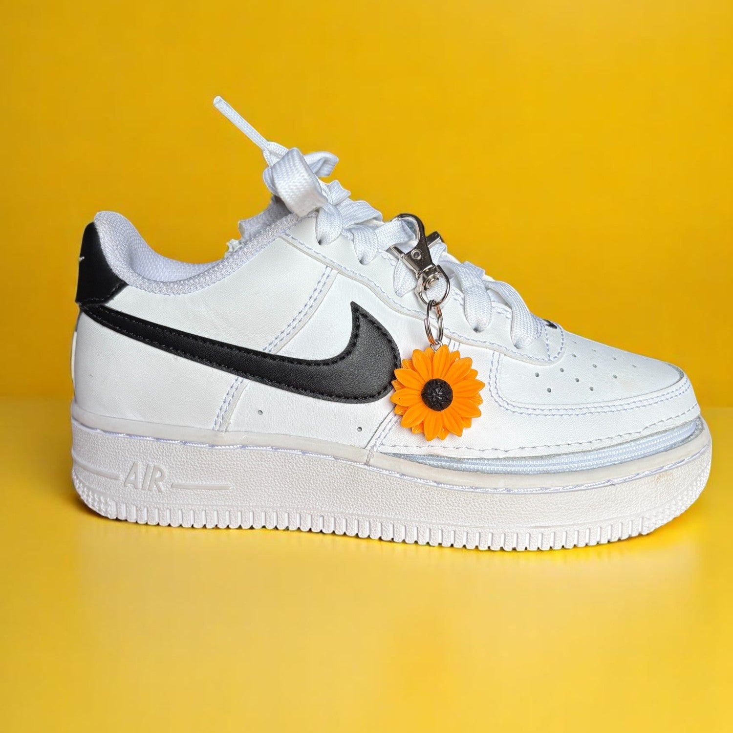 White sneaker with black Nike logo and orange flower charm on a yellow background