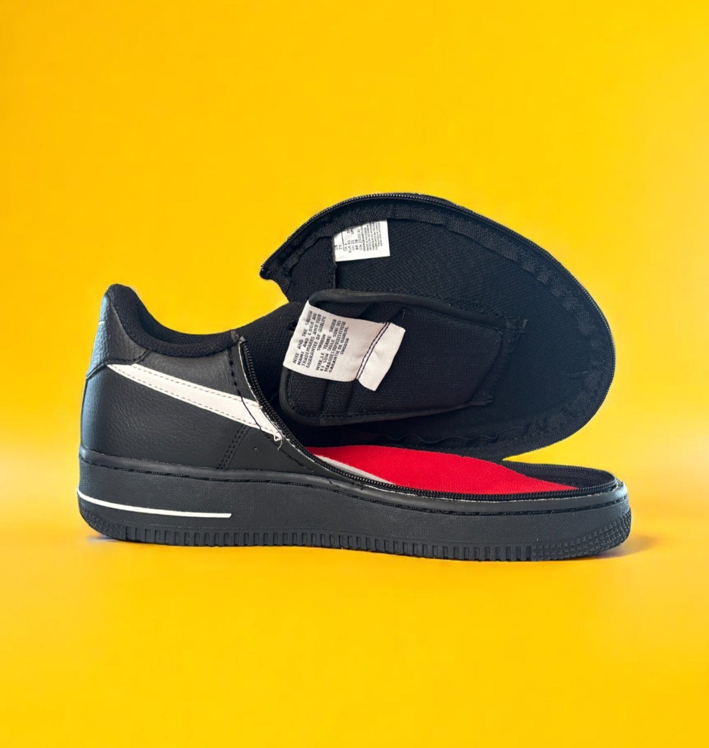 Kids black Nike shoe with a zipper on yellow background. The shoe is fully open