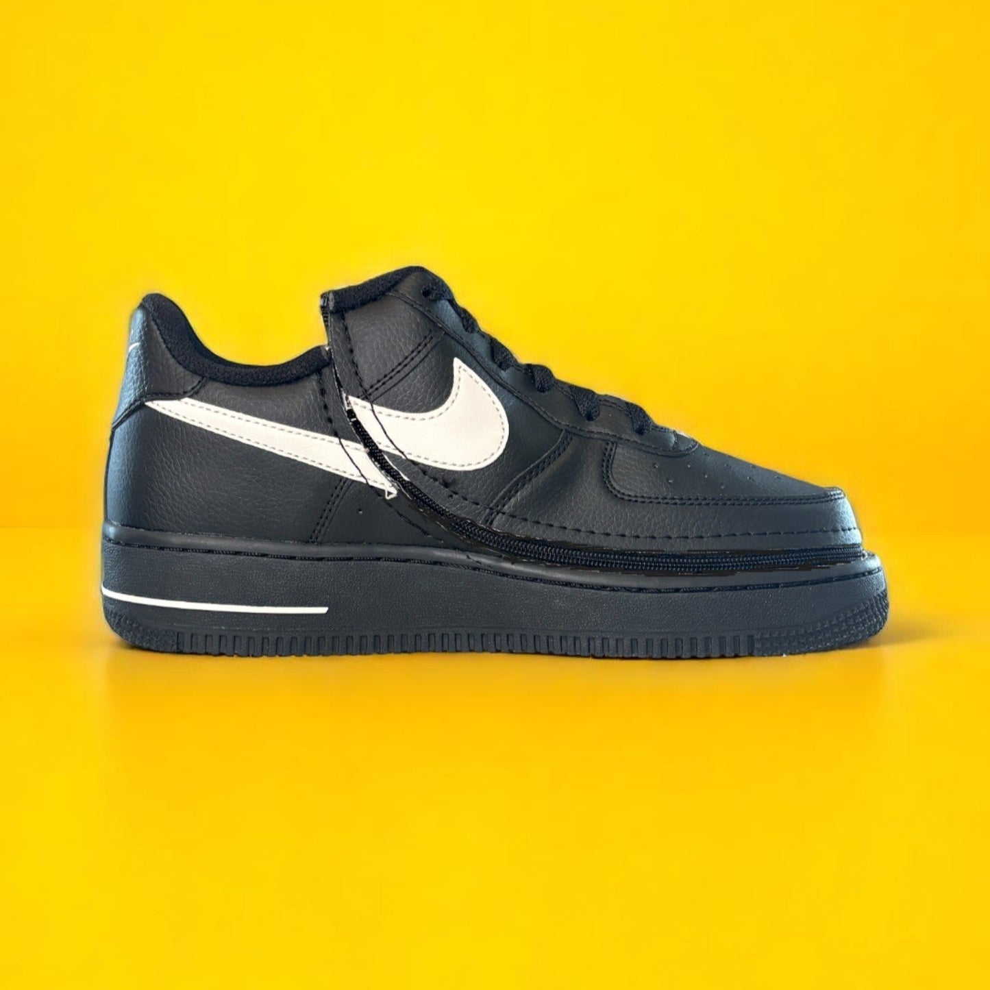 Kids black Nike shoe with a zipper on yellow background. The shoe is zipped shut